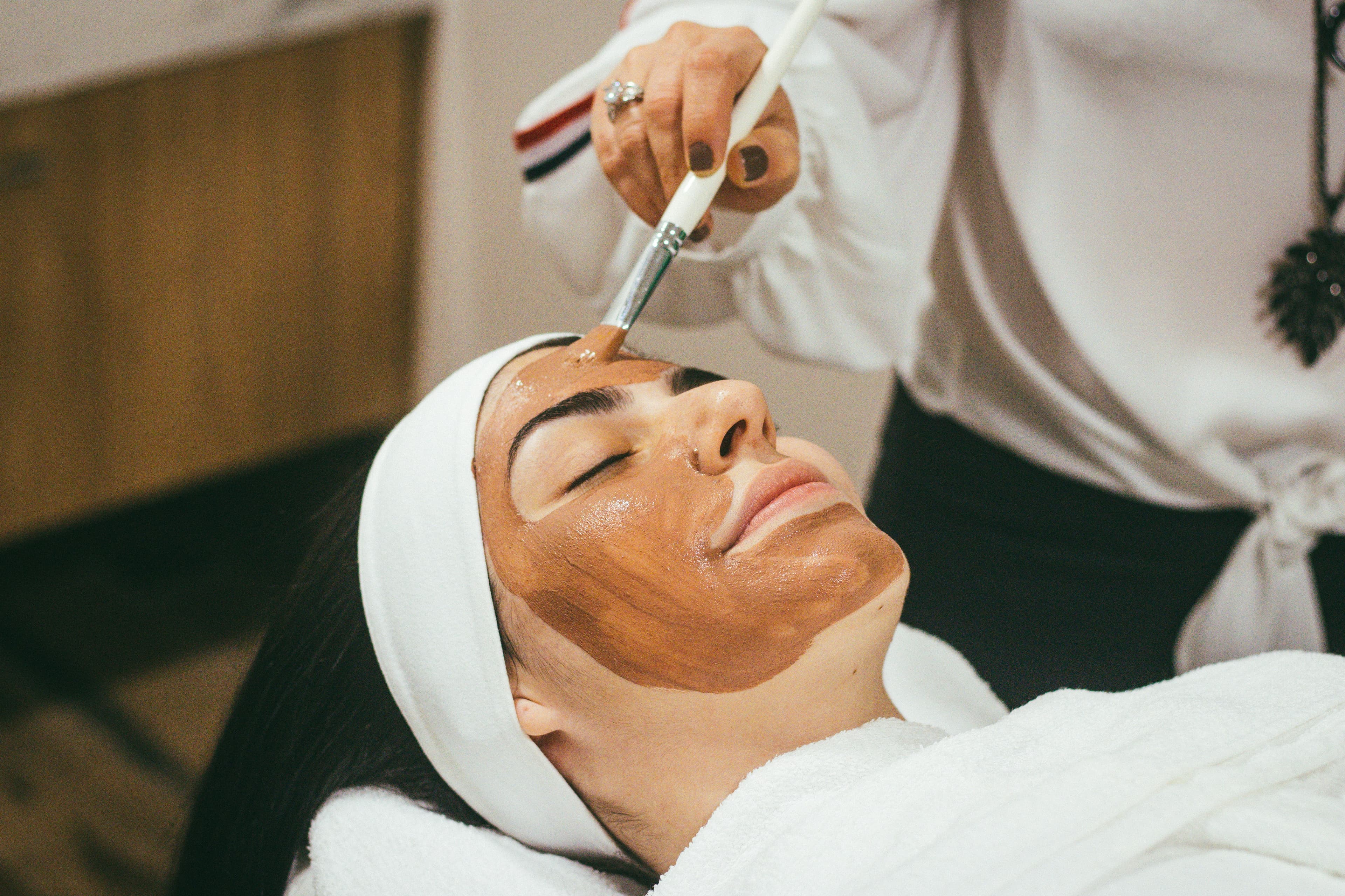 Cliente en soin de la peau dans un institut lumineux, esthéticienne appliquant un produit